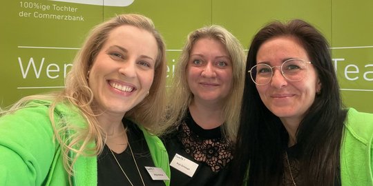 drei Frauen die freundlich in die Kamera lächeln vor der Messewand