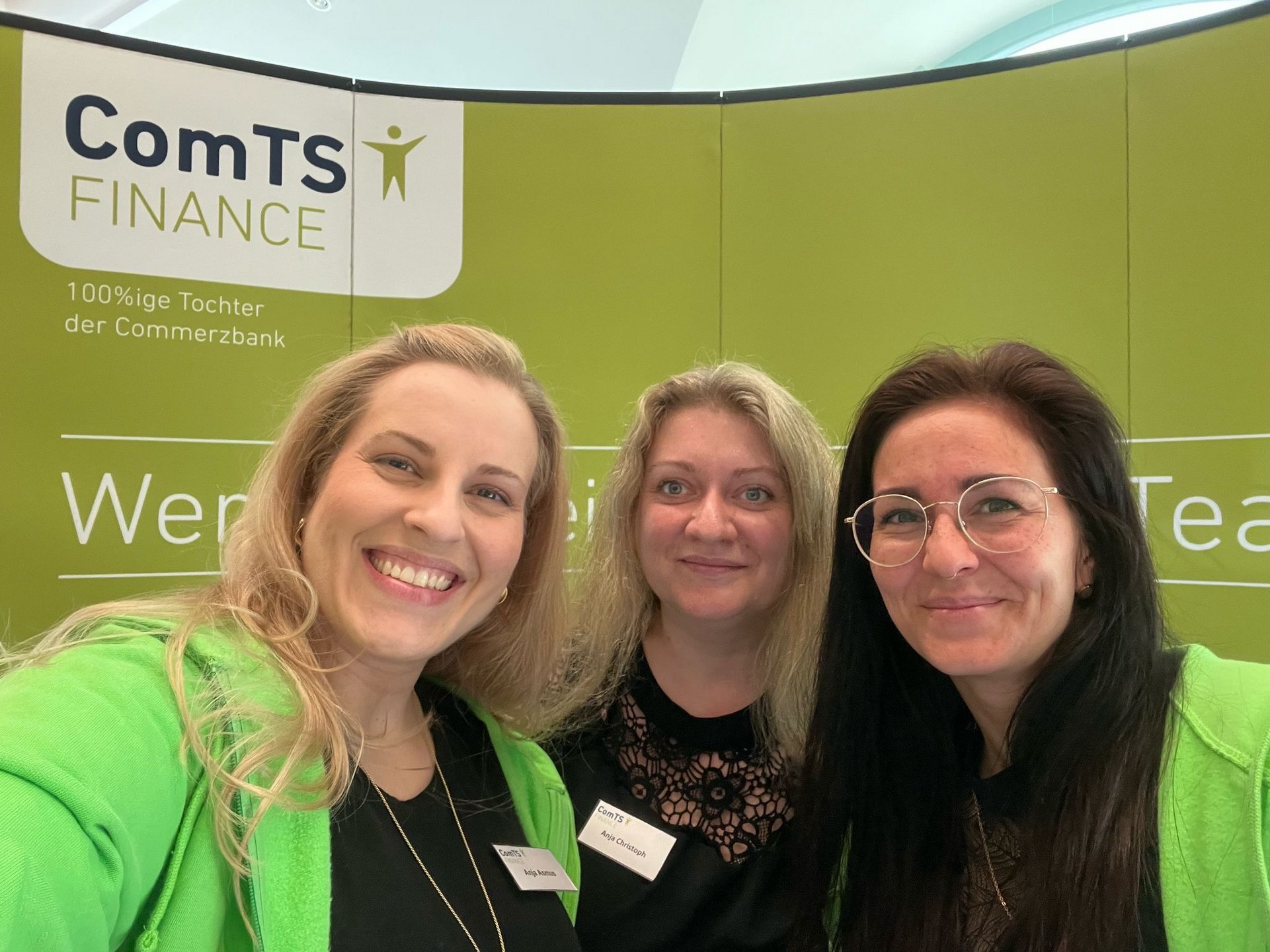 drei Frauen die freundlich in die Kamera lächeln vor der Messewand